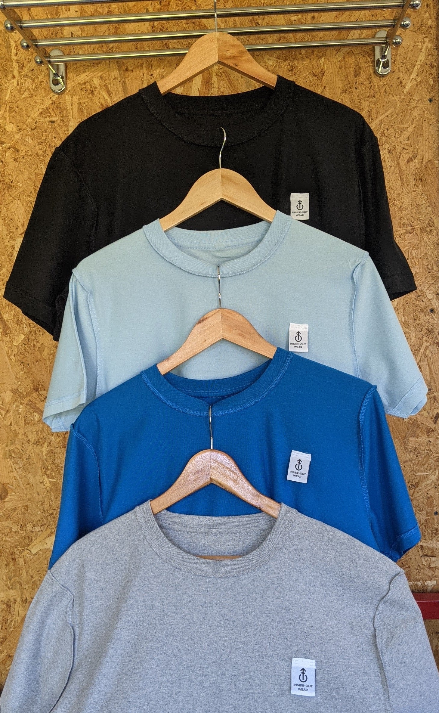 Four shirts in black, blue, gray, and light blue hanging on a wooden wall.
