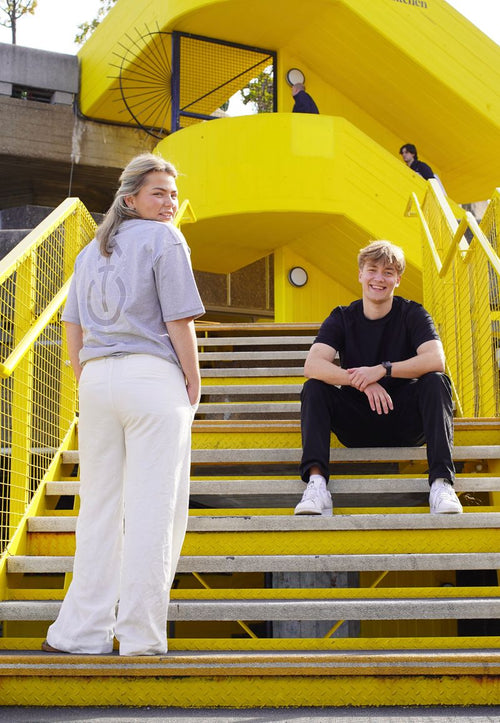Two people sitting on yellow steps with a bright yellow architectural structure in the background